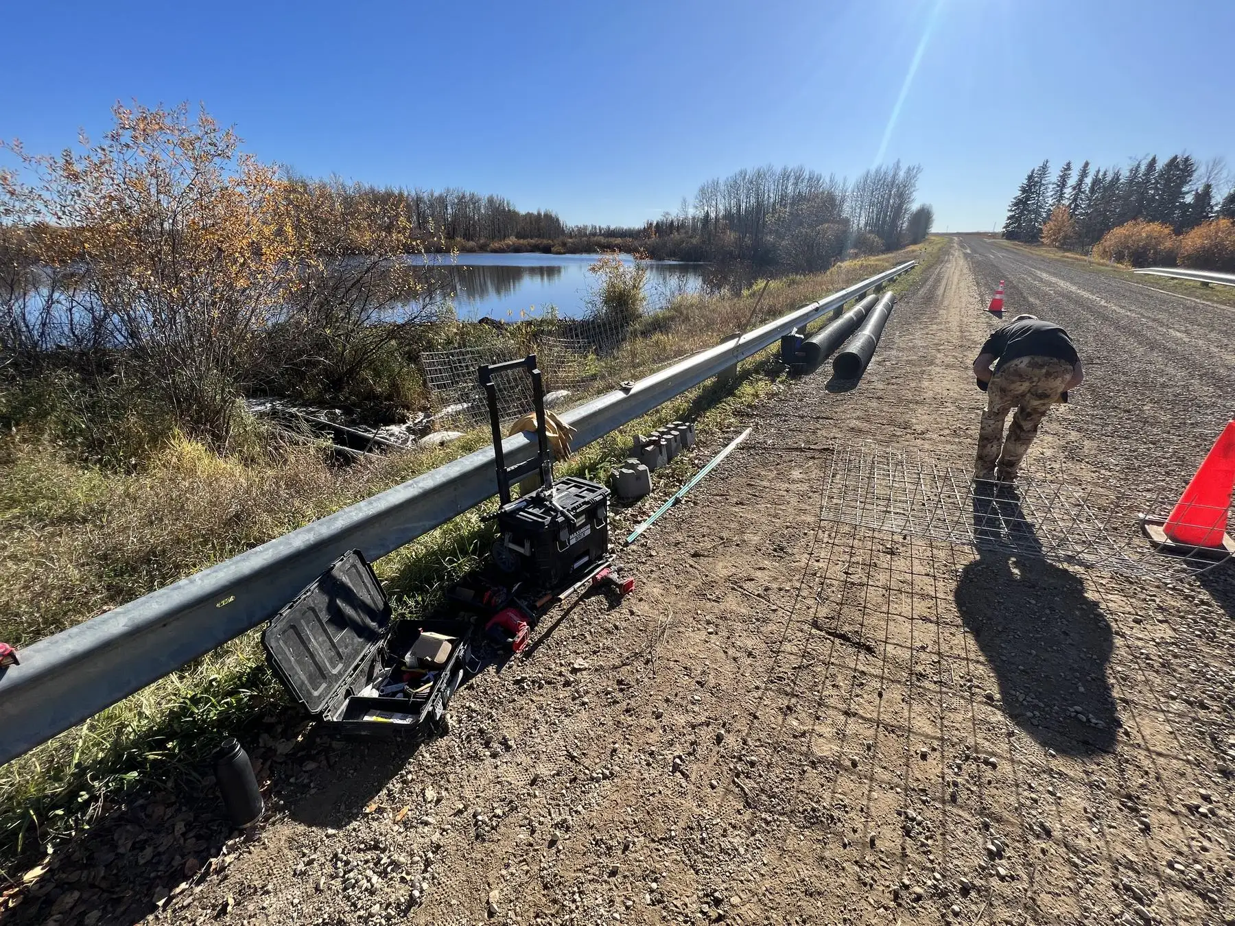 Crew and equipment on a gravel road beside a pond during a flow device install