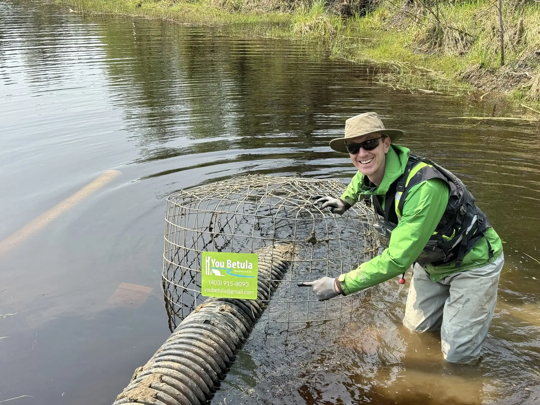 A crew member in waders beside a pond leveller intake cage in open water